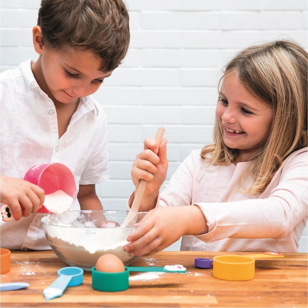 Bambino e bambina mescolano impasto con misurini e uovo in ciotola.
