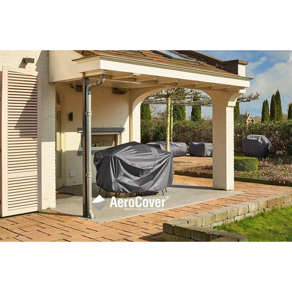 Gartenmöbel unter einer Terrassenüberdachung mit grauen Bezügen. Bäume und Büsche im Hintergrund.