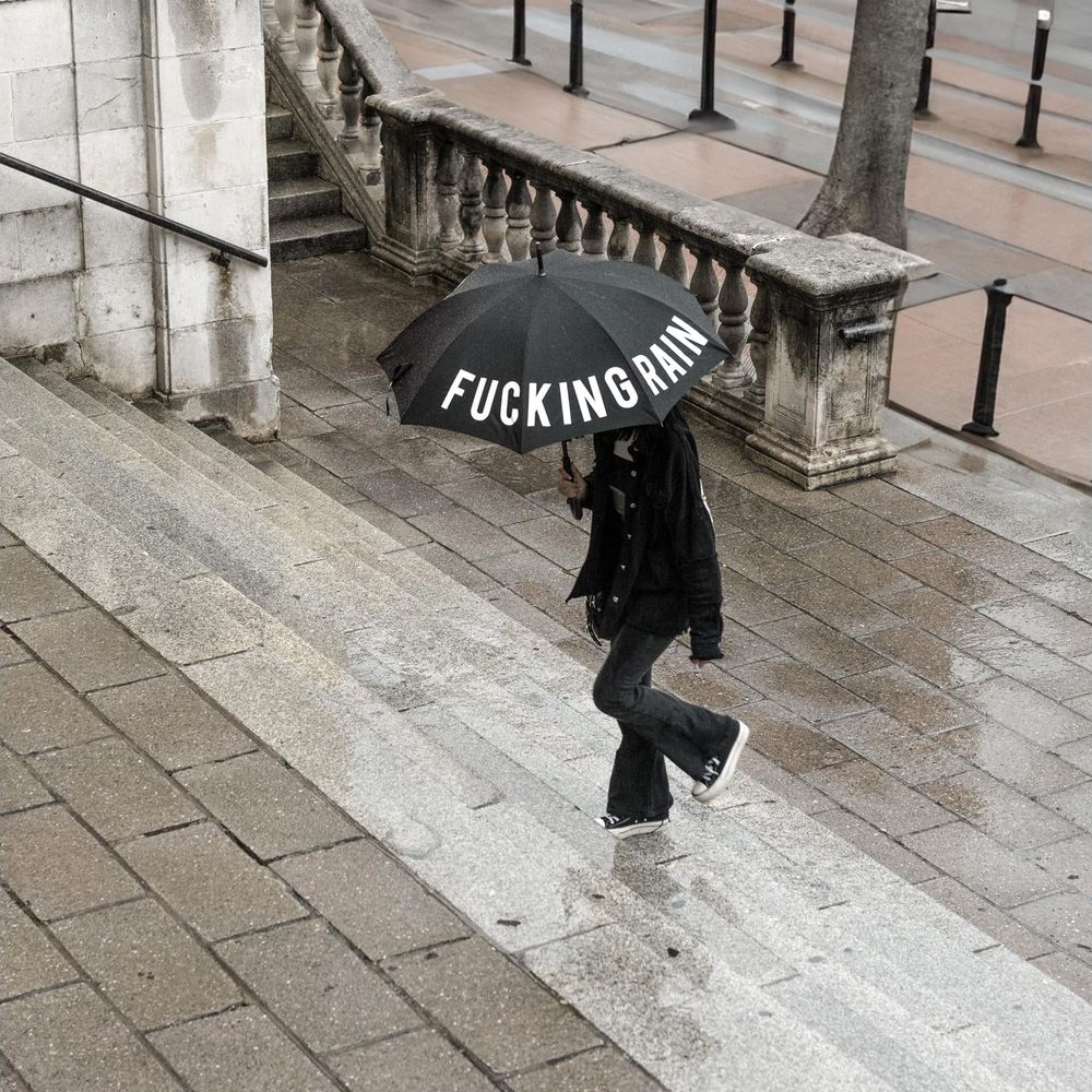 Person mit Regenschirm "FUCKING RAIN" geht nasse Treppe hinunter.