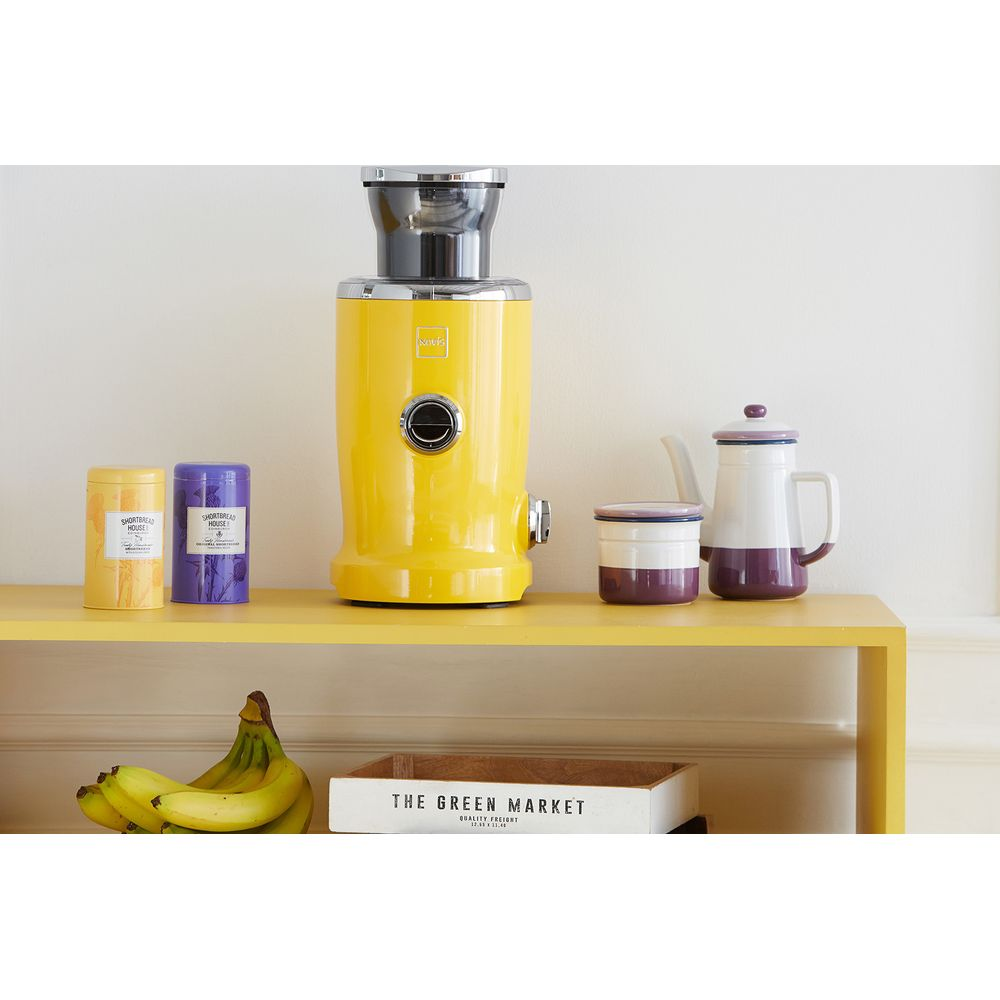 Juceuse jaune avec boîtes, pichet et bananes sur une étagère.