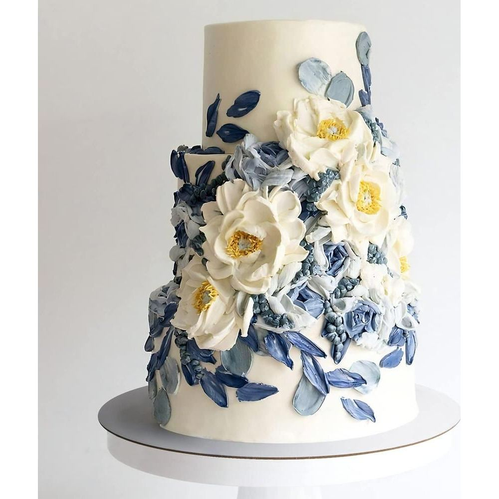 Creme-Torte mit weißen und blauen Blumenverzierungen, auf einem weißen Ständer.
