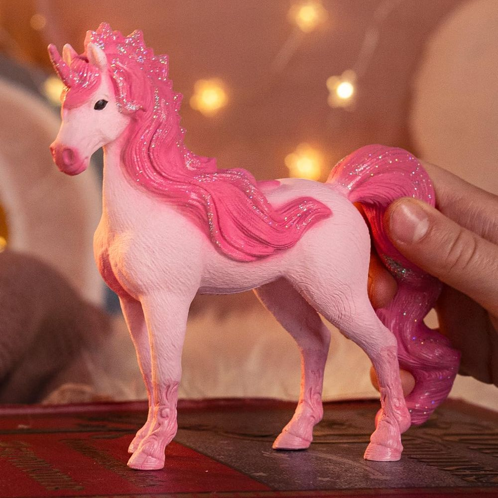Eine Person hält einen rosafarbenen Einhorn-Spielzeugschwanz. Glitzer verziert Mähne und Schwanz.