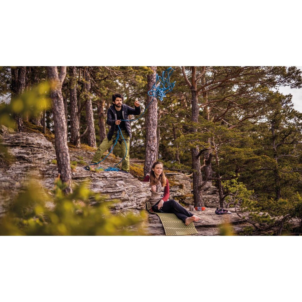 Mann mit Seil auf felsiger Klippe mit Frau auf Matte im Wald sitzend.