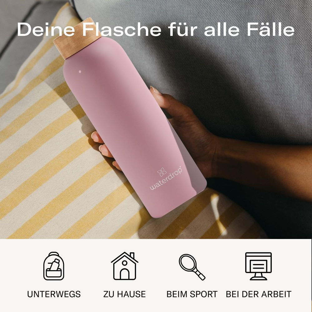 Eine rosafarbene Wasserflasche mit Holzdeckel wird von einer Hand gehalten.