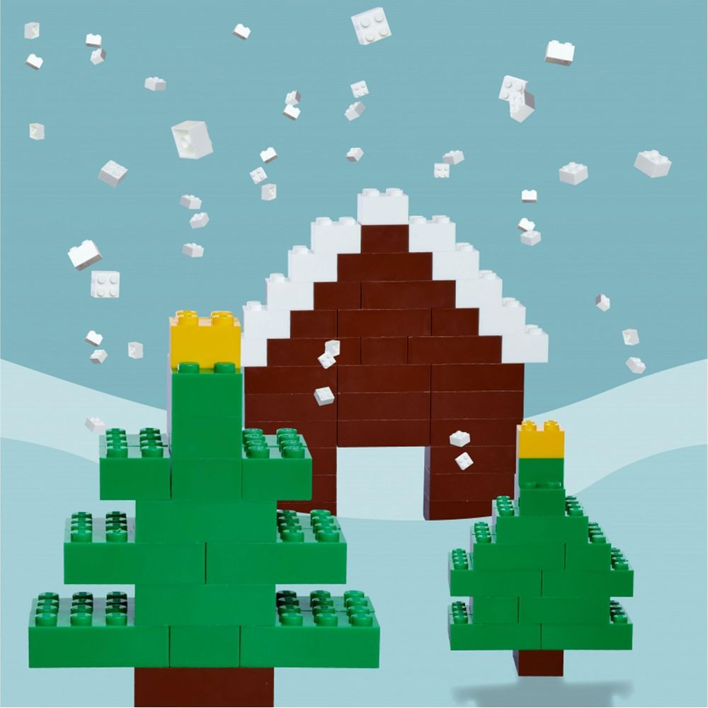 Lego-Haus und Bäume im Schnee. Weiße Steine fallen wie Schnee.