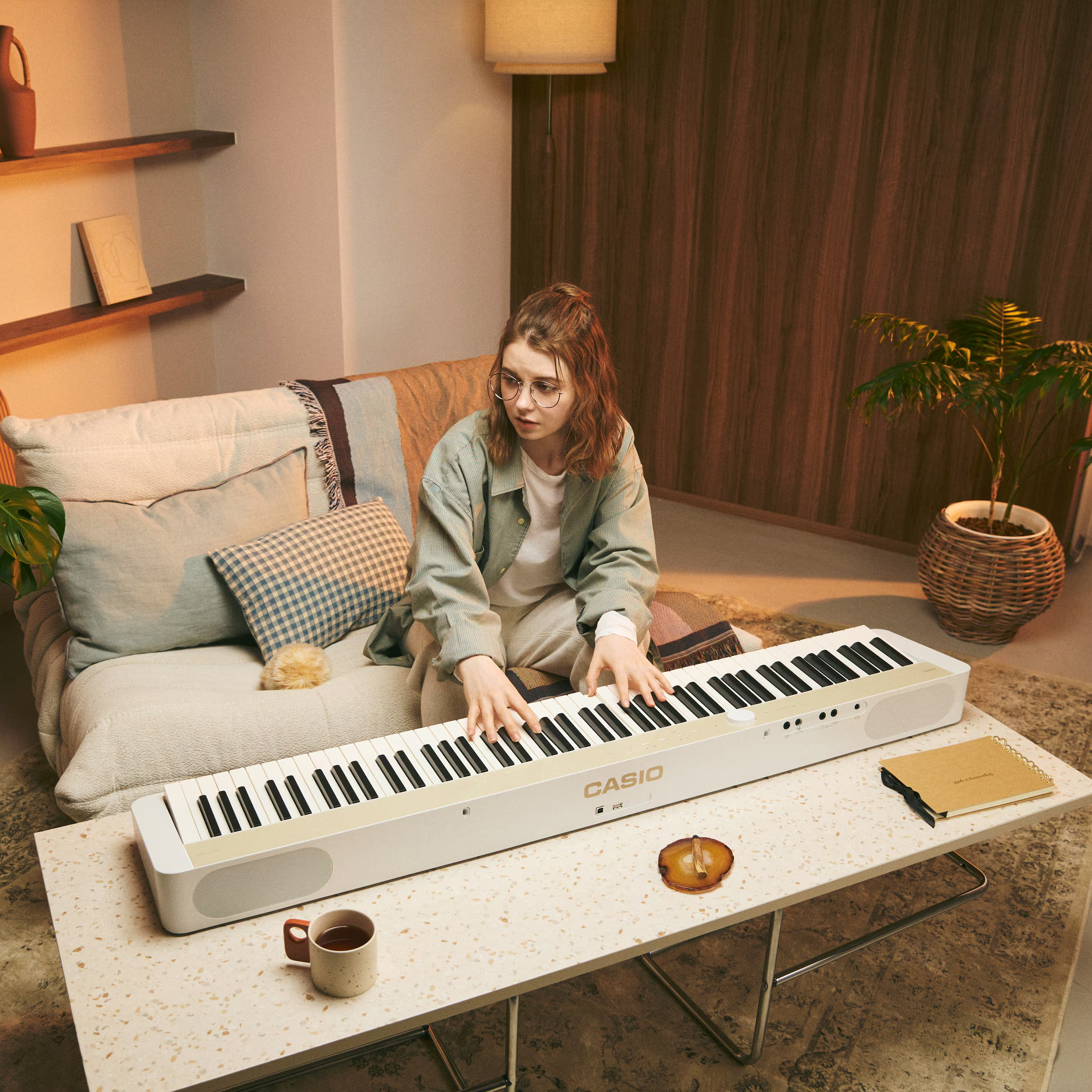 Eine junge Frau mit Brille spielt auf einem weißen Casio-Keyboard, das auf einem Tisch steht.