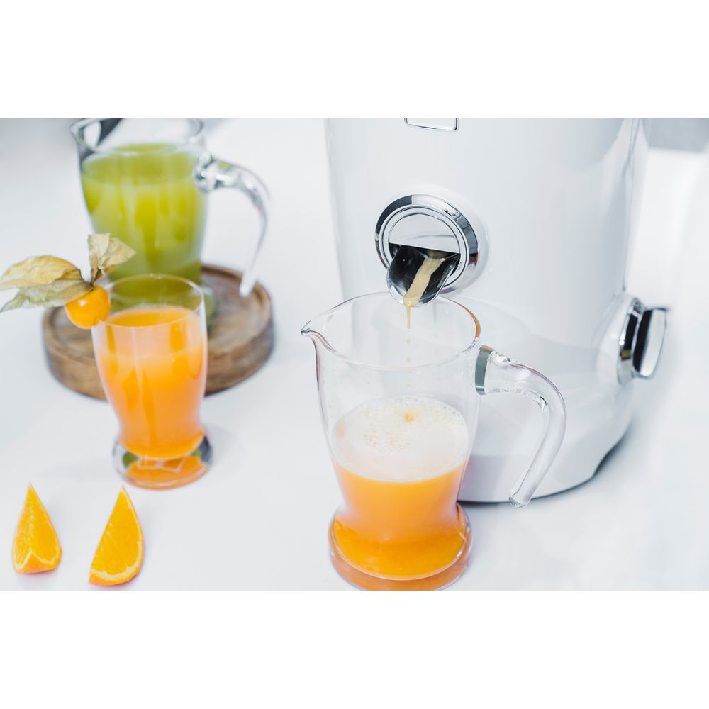 Ein Entsafter presst Orangensaft in ein Glas. Zwei Orangenscheiben liegen daneben.