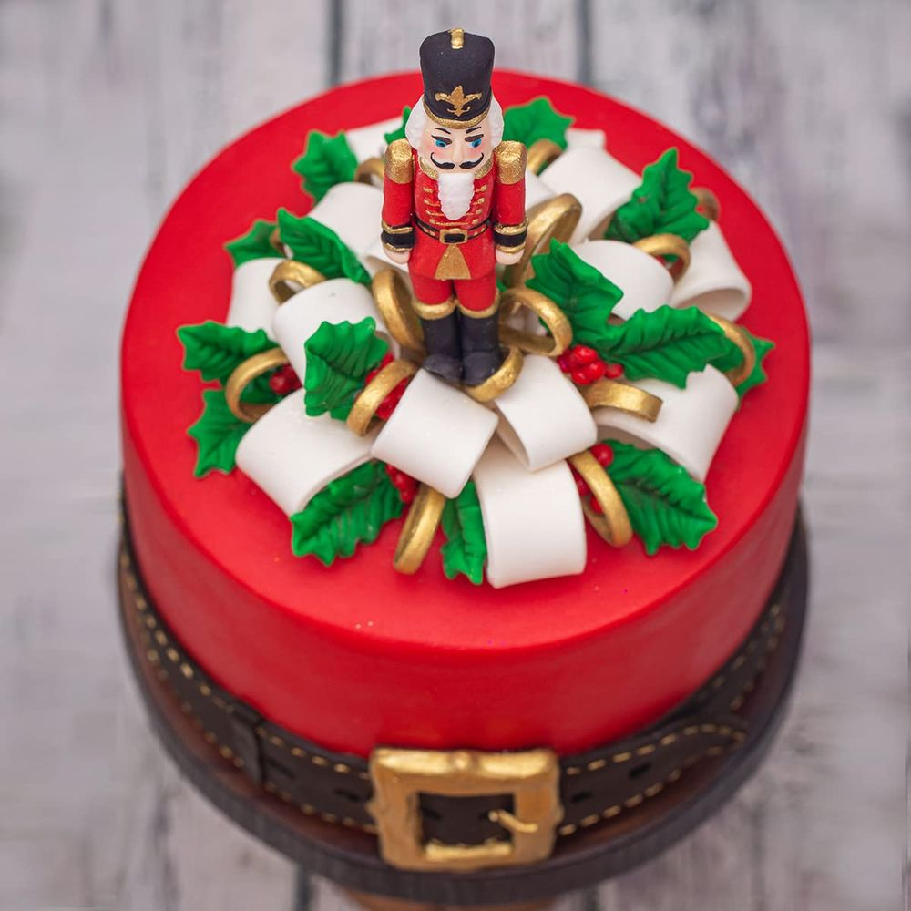 Ein rot glasierter Kuchen mit einem Nussknacker, weißen Schleifen und Stechpalmenblättern.