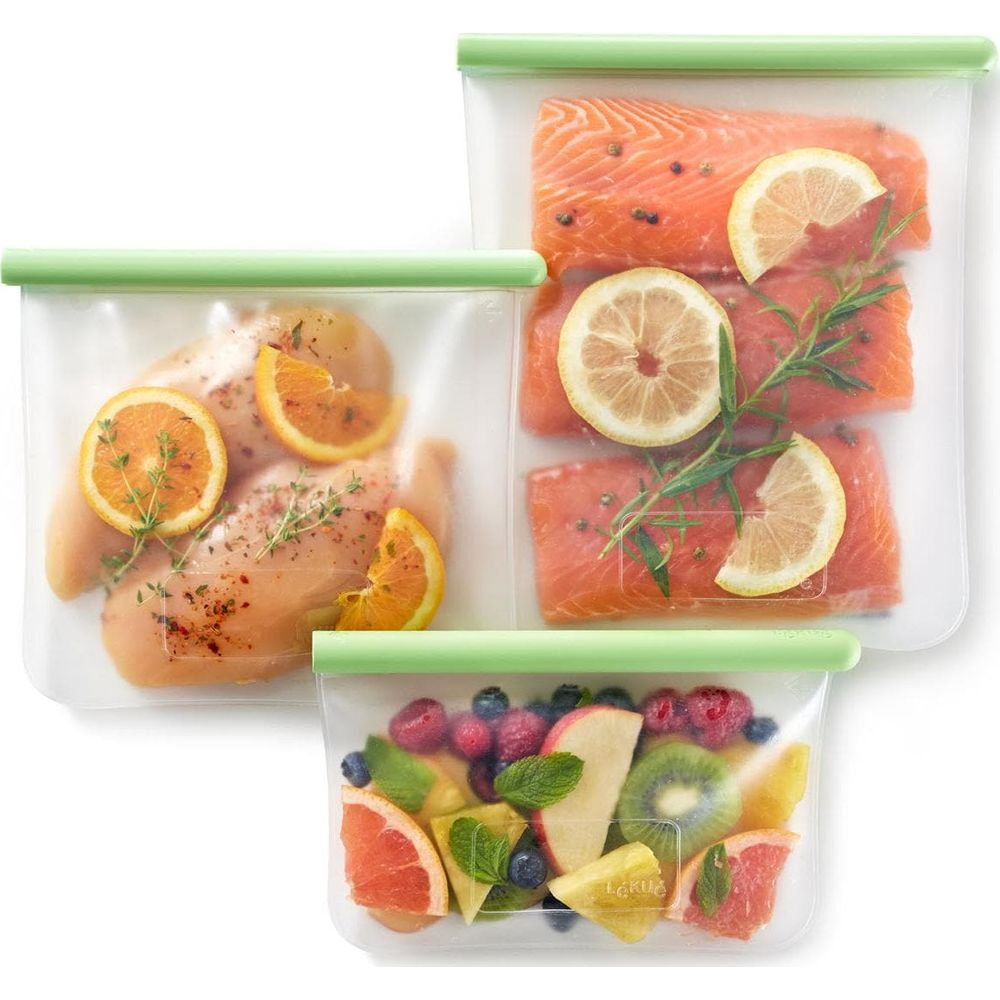 Drei wiederverwendbare Beutel mit Lebensmitteln: Hähnchen, Lachs und Obstsalat.