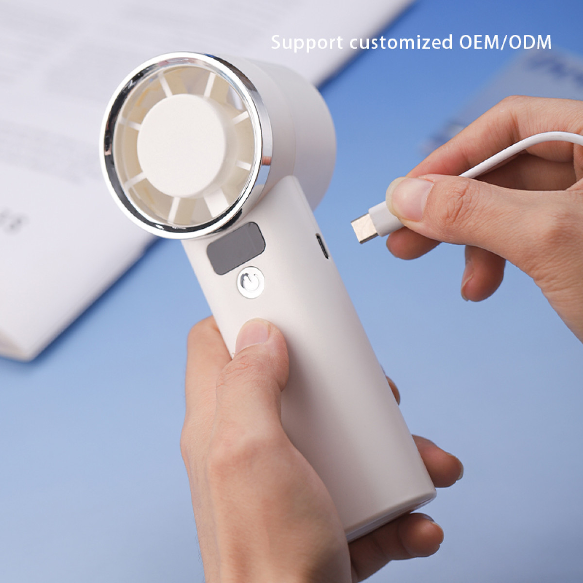 Hände verbinden ein weißes USB-C-Kabel mit einem weißen tragbaren Ventilator.