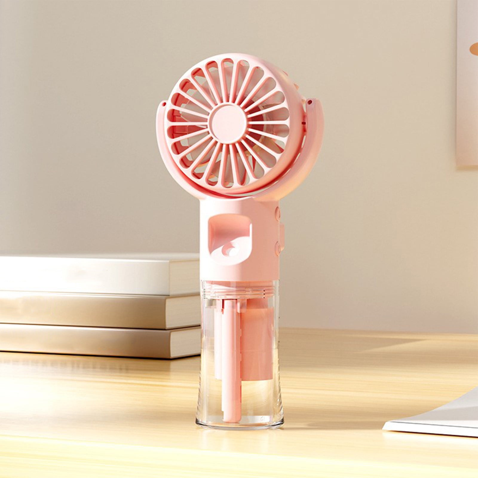 Ein rosafarbener Handventilator mit transparentem Behälter steht auf einem Holztisch.