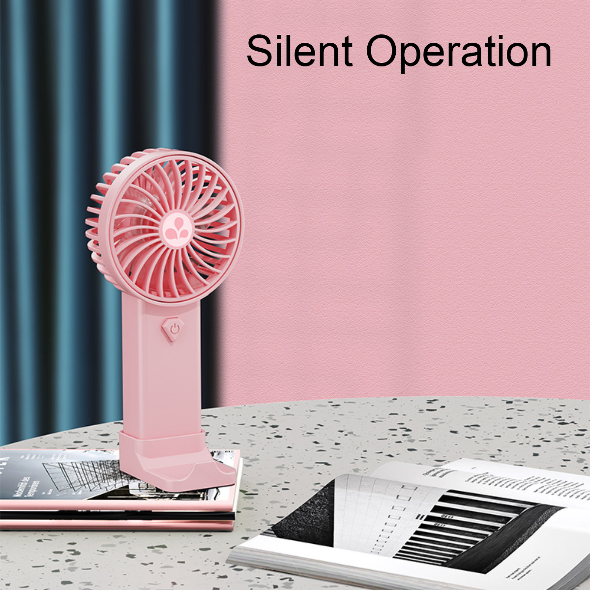 Ein pinker tragbarer Ventilator sitzt neben Büchern auf einem Tisch. Text: 'Silent Operation'.