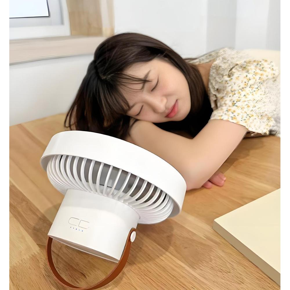 Eine Frau schläft auf einem Tisch neben einem weißen Ventilator.