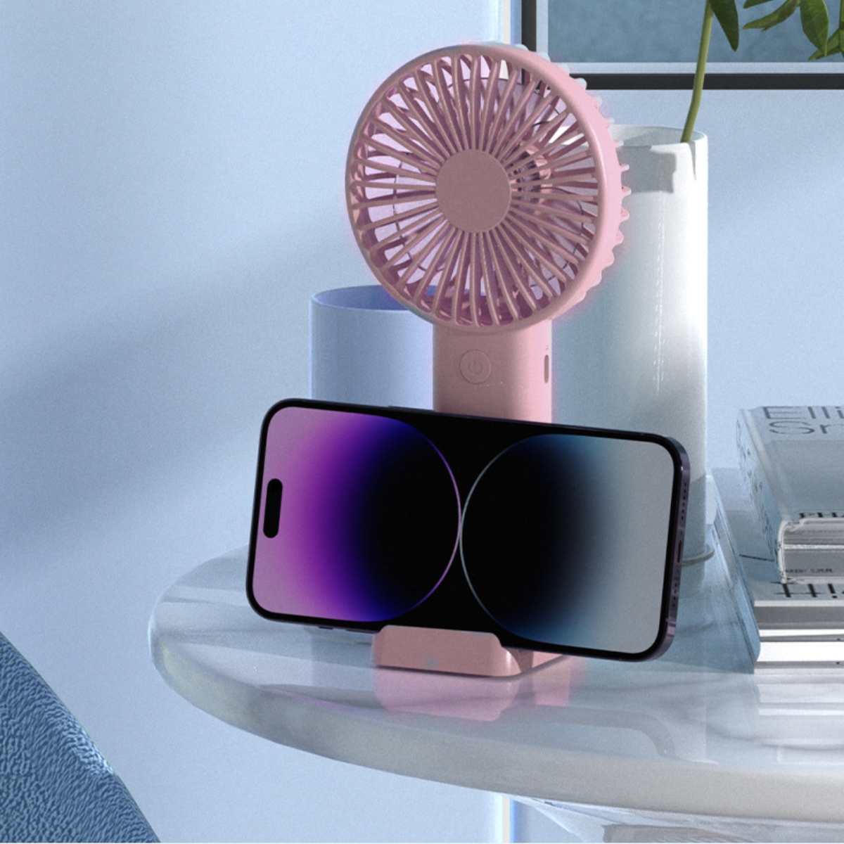 Ein rosafarbener Handventilator steht hinter einem Smartphone auf einem rosafarbenen Ständer.