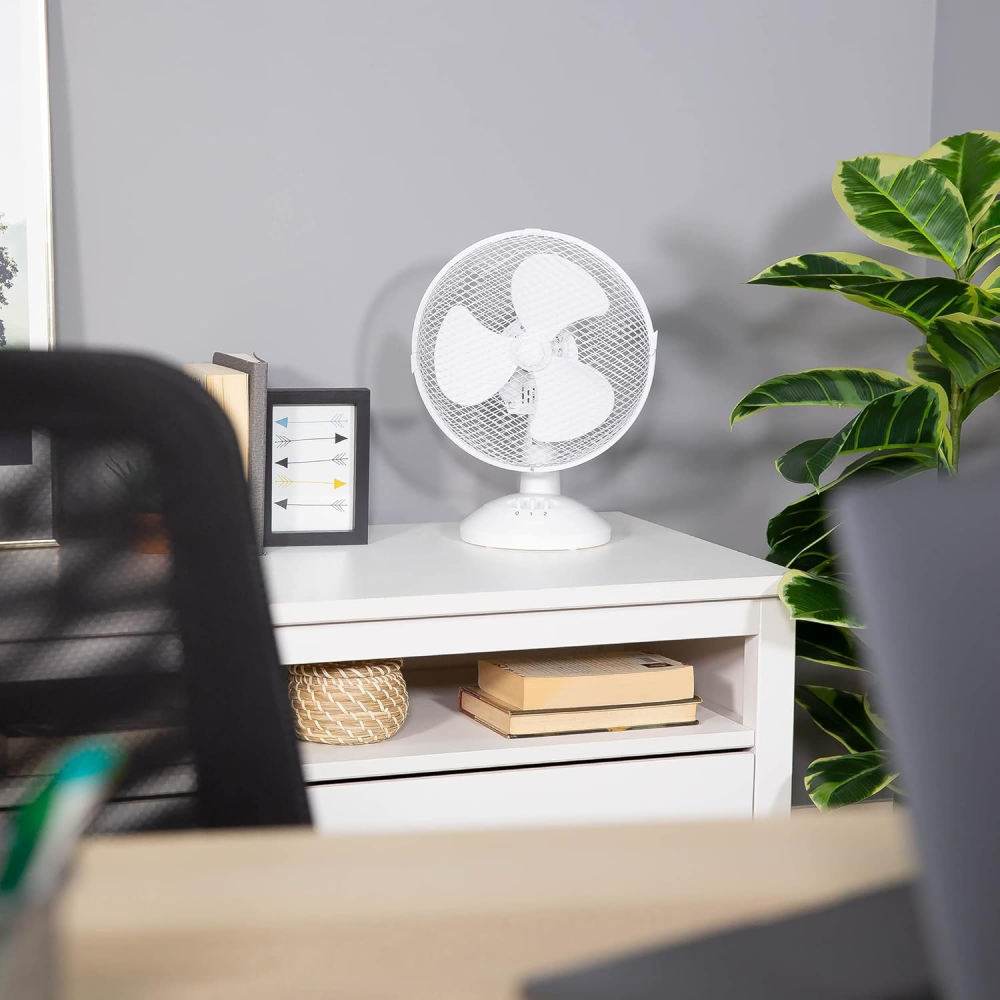 Ein weißer Schreibtischventilator steht neben Büchern und einer Pflanze auf einem weißen Schrank.