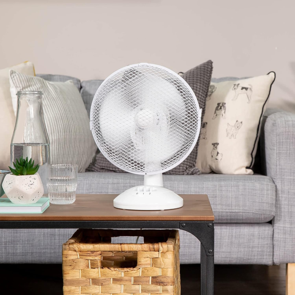 Ein weißer Tischventilator steht auf einem Holztisch vor einem Sofa.