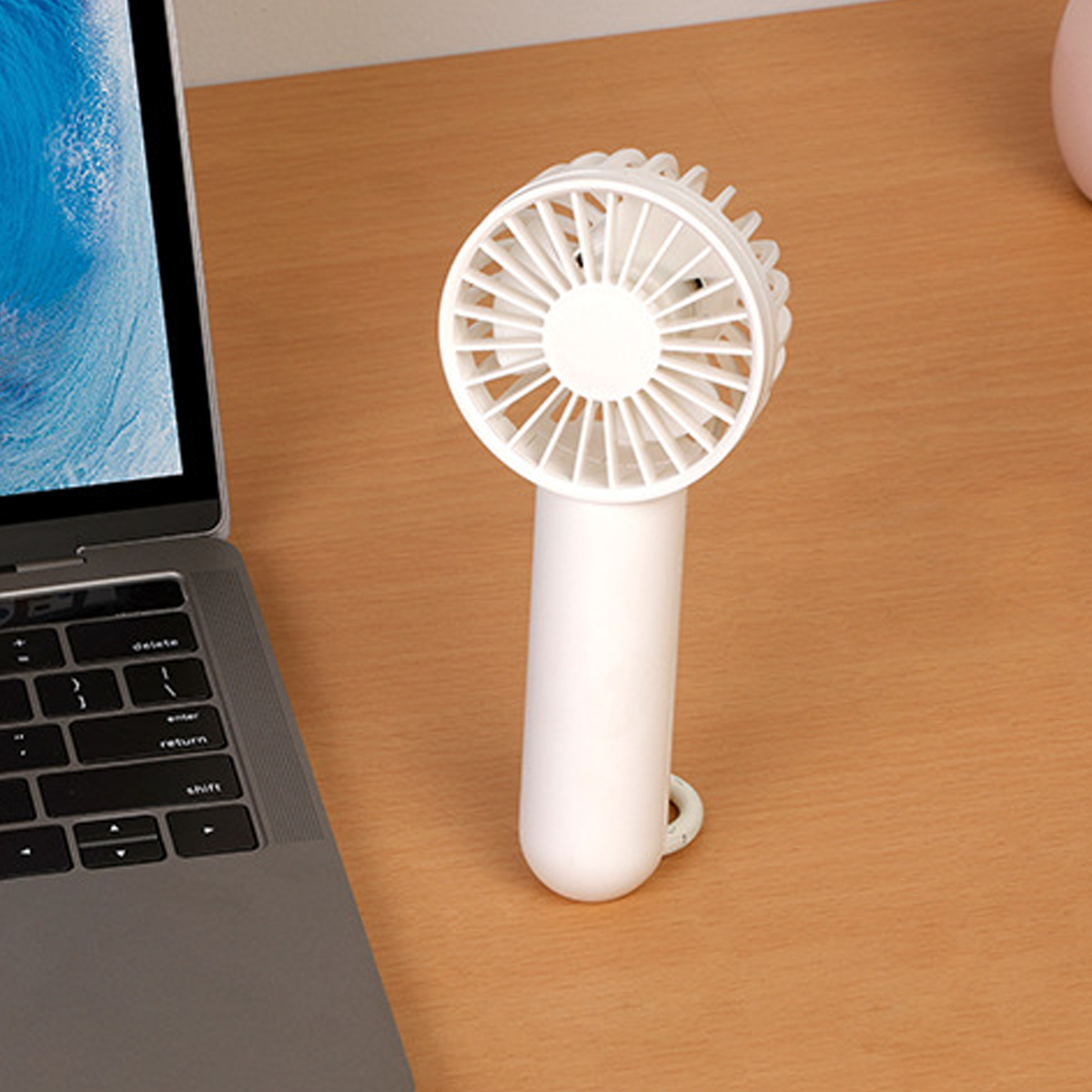 Ein weißer Handventilator steht neben einem Laptop auf einem Holztisch.