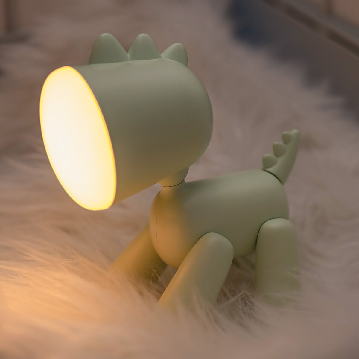 Eine hellgrüne Lampe in Dinosaurierform sitzt auf einer flauschigen weißen Oberfläche.