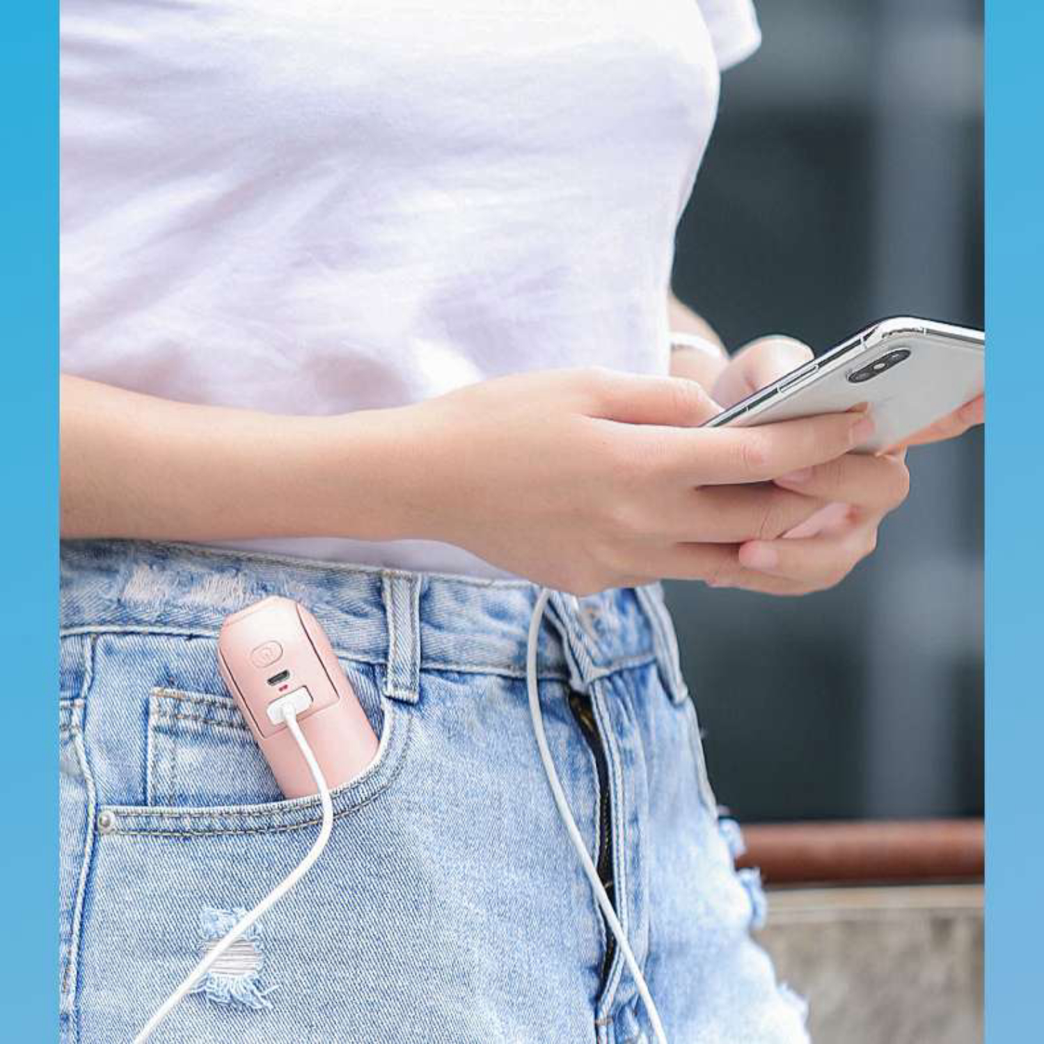 Eine Person in Jeans und weißem T-Shirt benutzt ein Handy, ein rosa Ladegerät steckt in der Hosentasche.