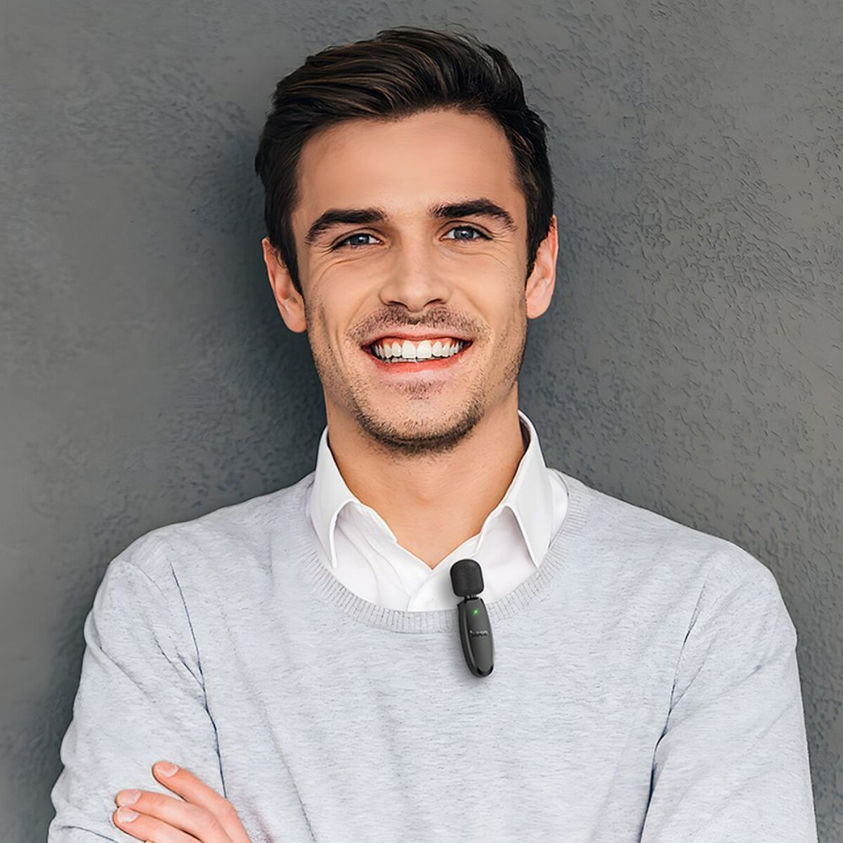 Un uomo con un microfono sul colletto, di fronte a un muro grigio.
