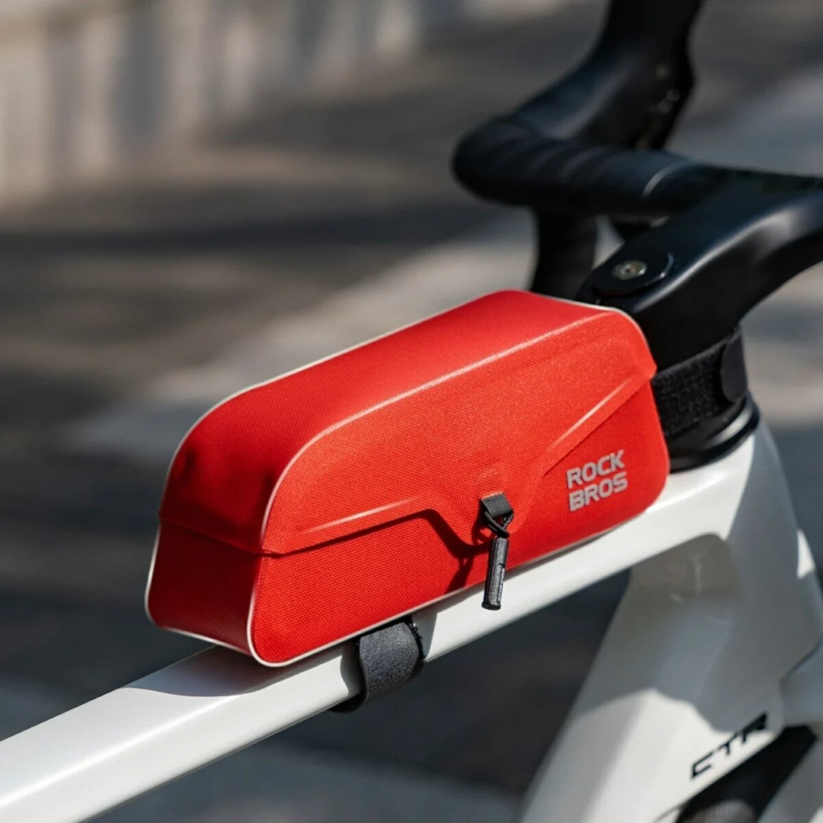 Rote ROCK BROS Fahrradtasche am Rahmen befestigt, mit weißem Besatz und schwarzem Reißverschlusszieher.