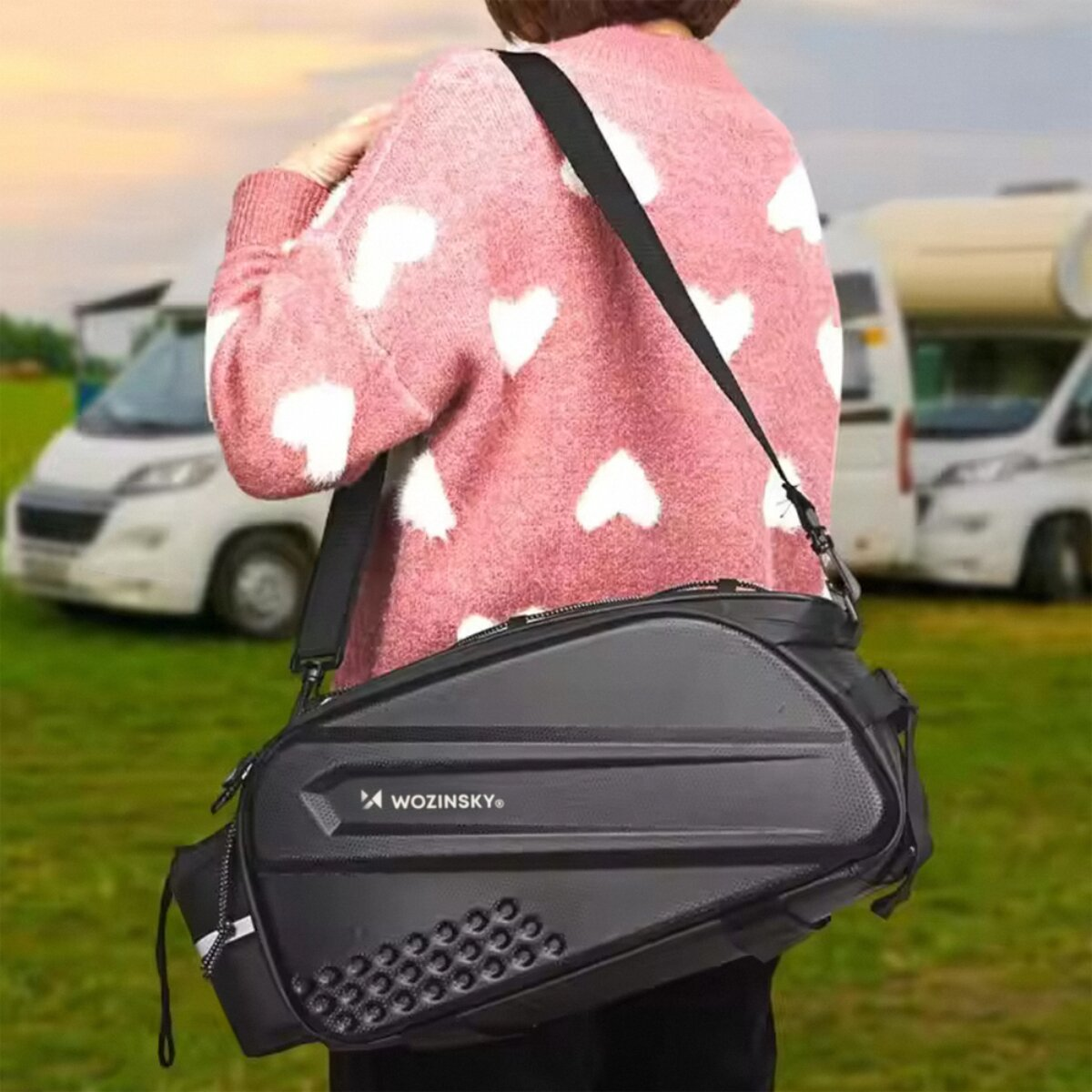 Person mit schwarzer Tasche, rosafarbenem Pullover mit Herzen, Wohnmobile im Hintergrund.