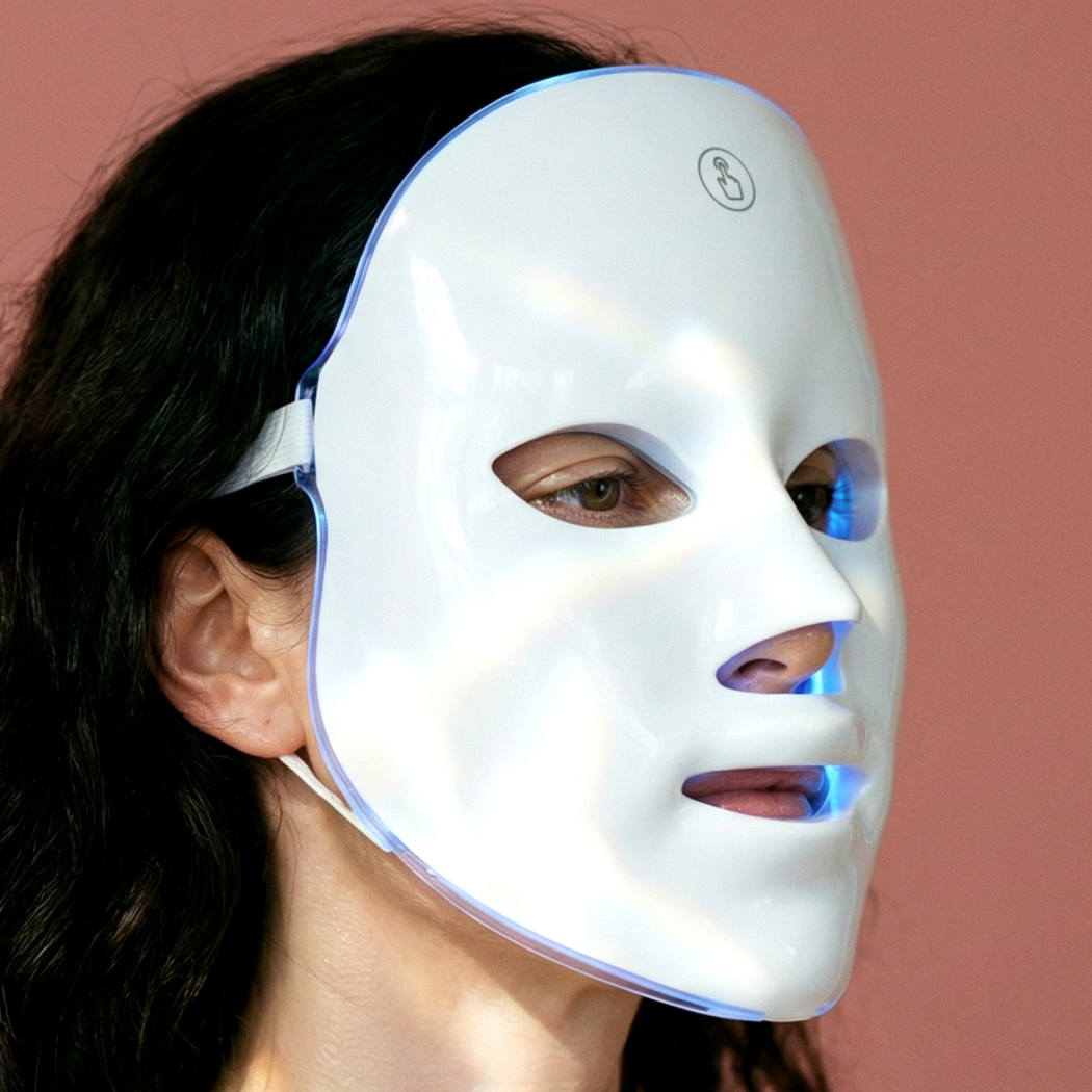 Biała maska LED z niebieskimi światłami noszona przez osobę z ciemnymi włosami.