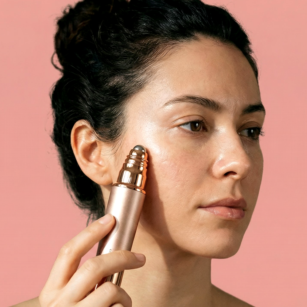 Kobieta z ciemnymi włosami aplikuje na policzek urządzenie do pielęgnacji skóry w kolorze różowego złota.