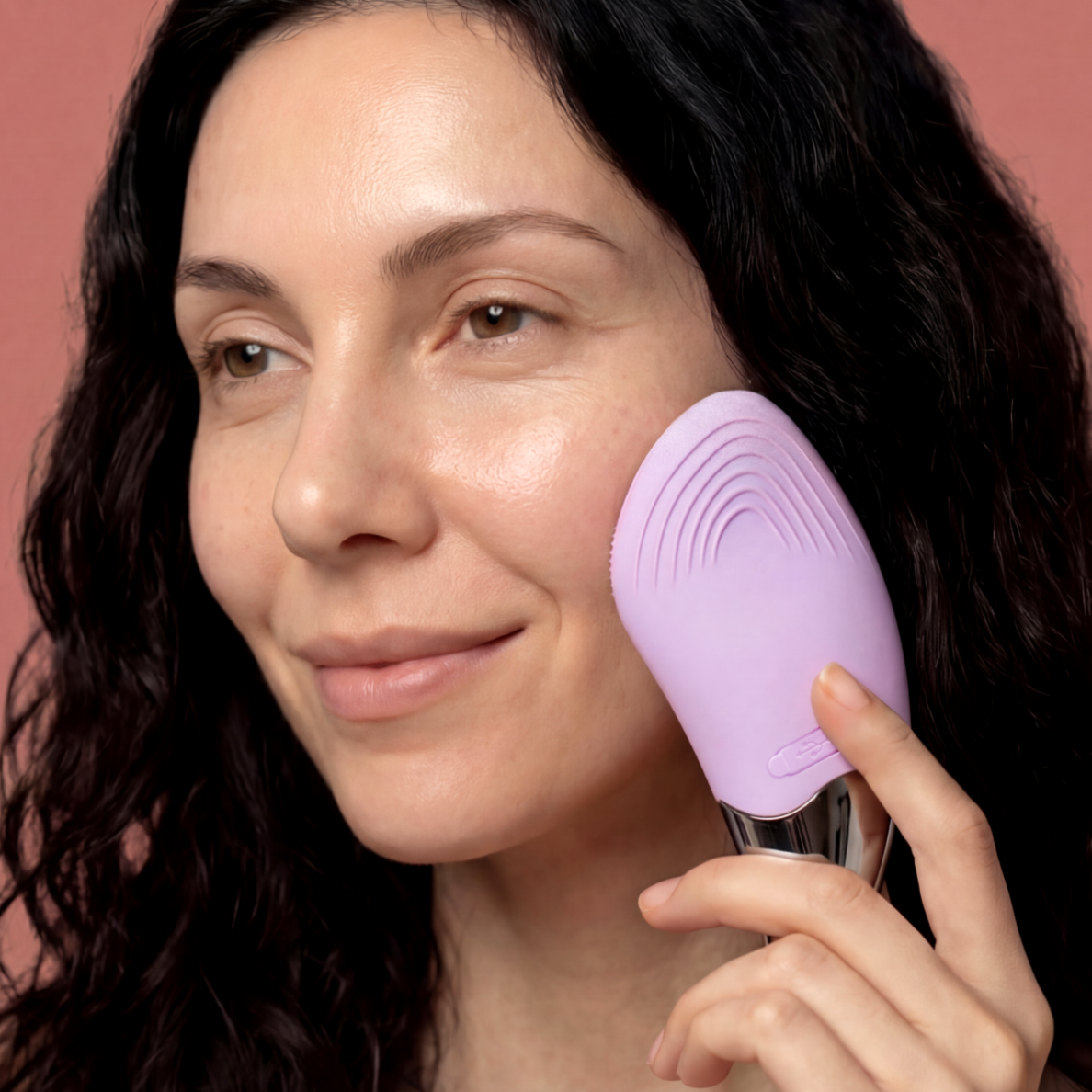 Kobieta z ciemnymi włosami używa fioletowego urządzenia do pielęgnacji twarzy.