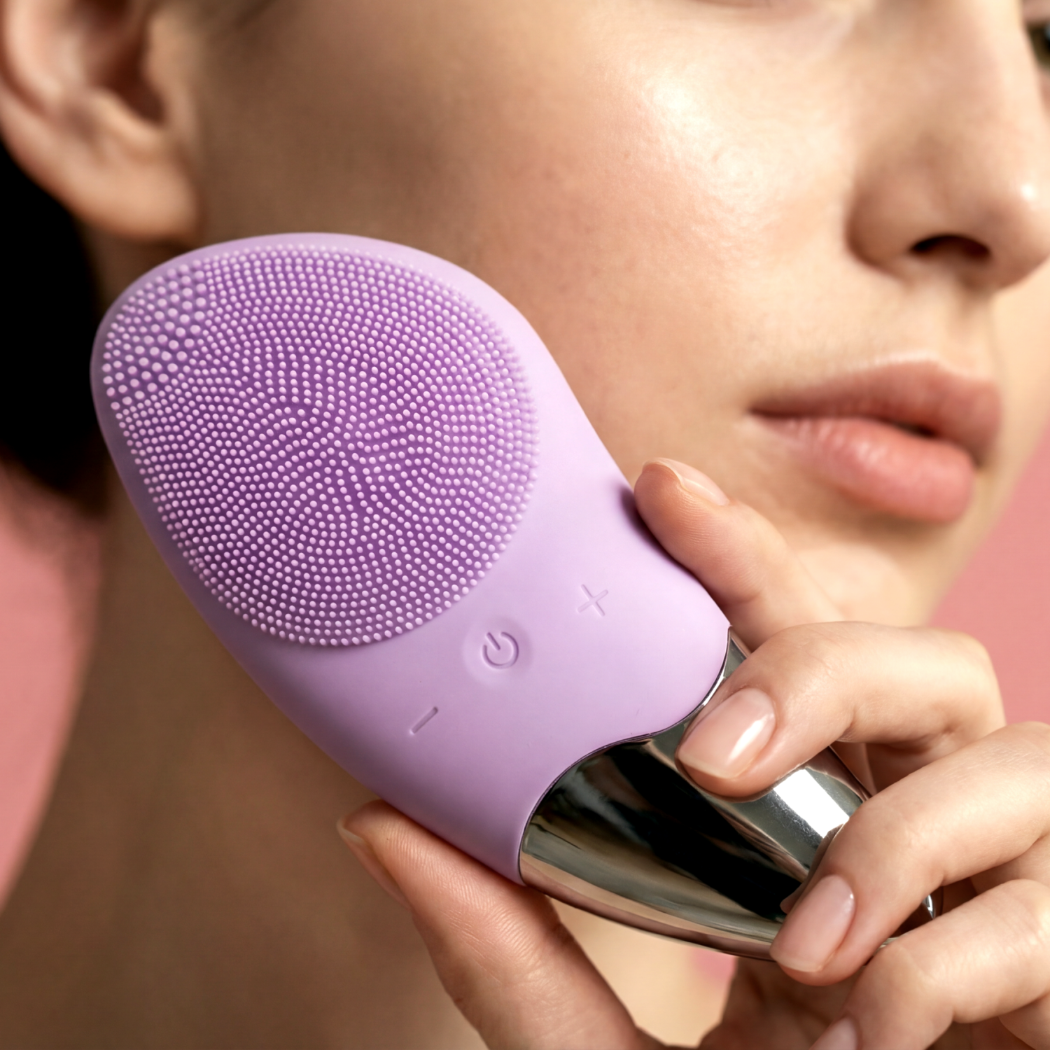 Kobieta trzyma fioletowe urządzenie do oczyszczania twarzy z silikonowymi włoskami blisko twarzy.