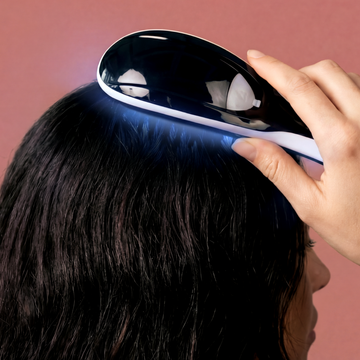 Una mano tiene un dispositivo bianco e nero sui capelli scuri, emettendo luce blu.