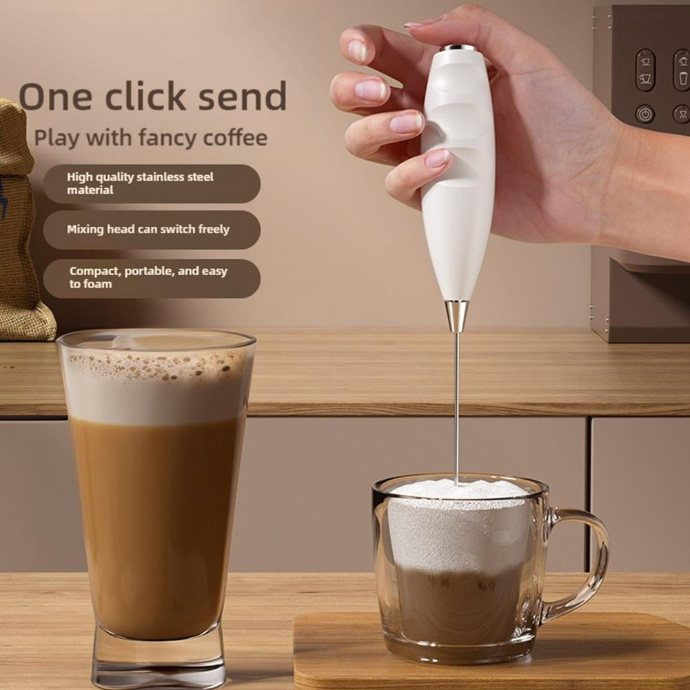 Ein weißer Milchaufschäumer schäumt Milch in einem Glasbecher neben einem hohen Glas Kaffee auf.