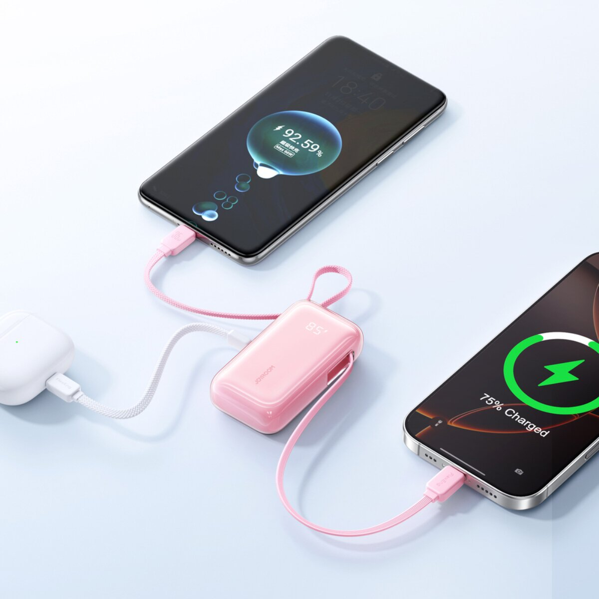 Ein rosa Powerbank lädt zwei Smartphones und eine weiße Ladehülle.