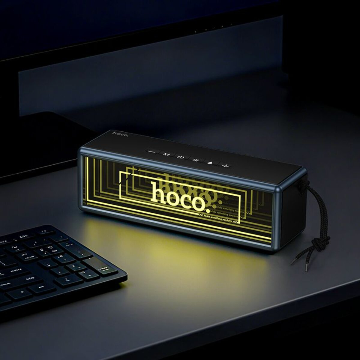 Schwarzer Lautsprecher mit gelber Beleuchtung und Hoco-Logo, neben einer Tastatur.