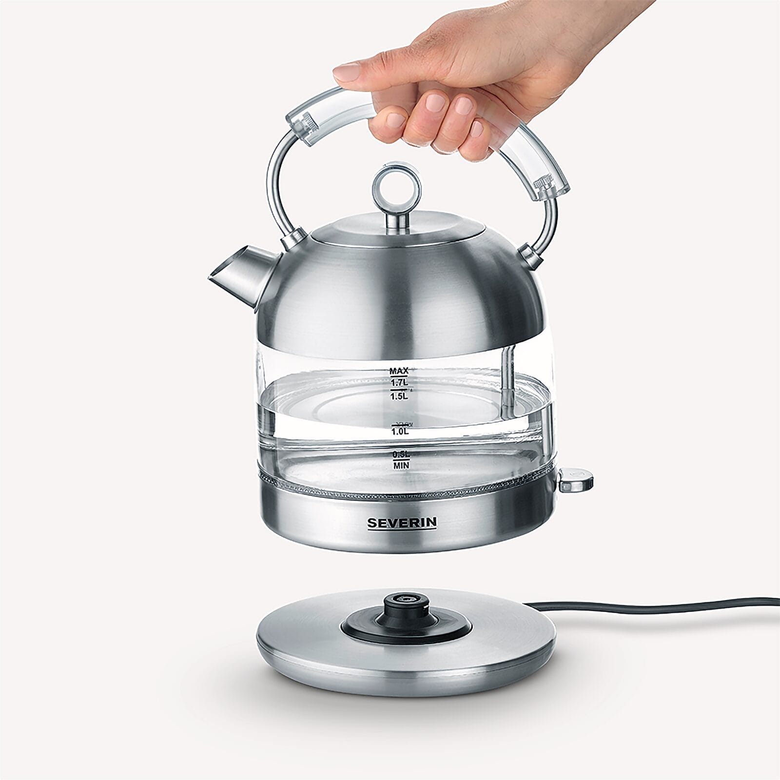 Ręka podnosi szklany czajnik elektryczny ze stali nierdzewnej z wodą z podstawy, na białym tle.
