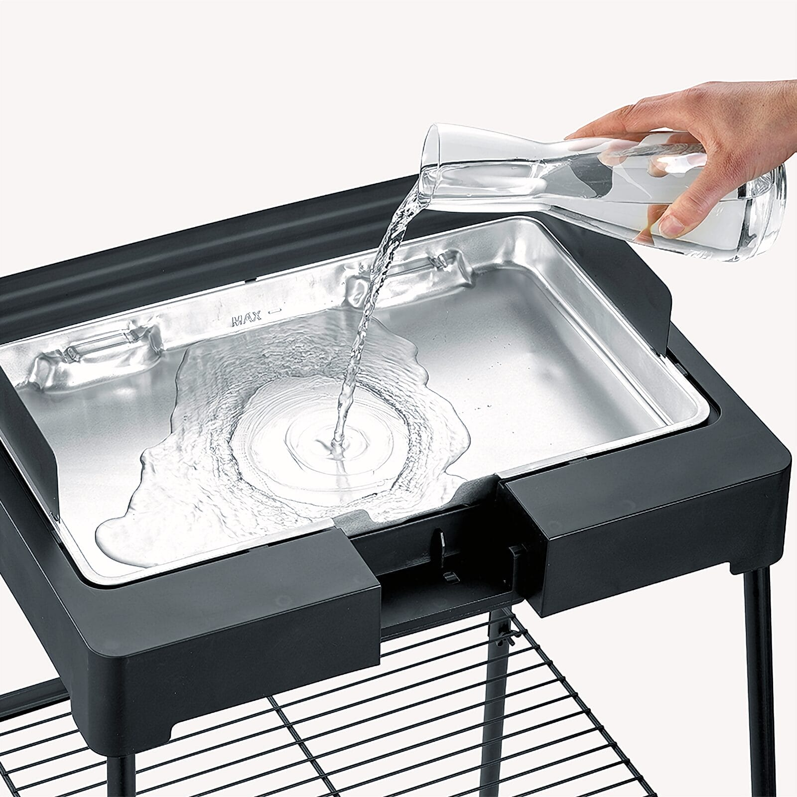 Water is being poured from a glass into a grill pan.