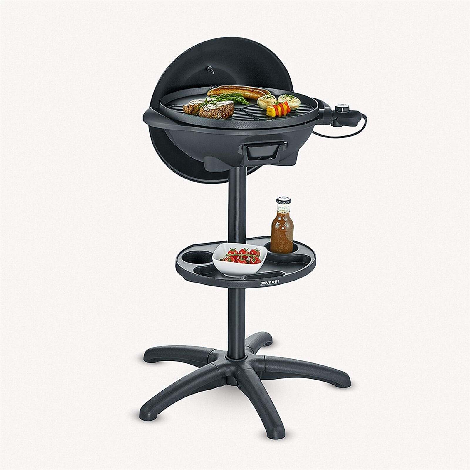 A black electric grill on a stand with meat, sausage, and vegetables.
