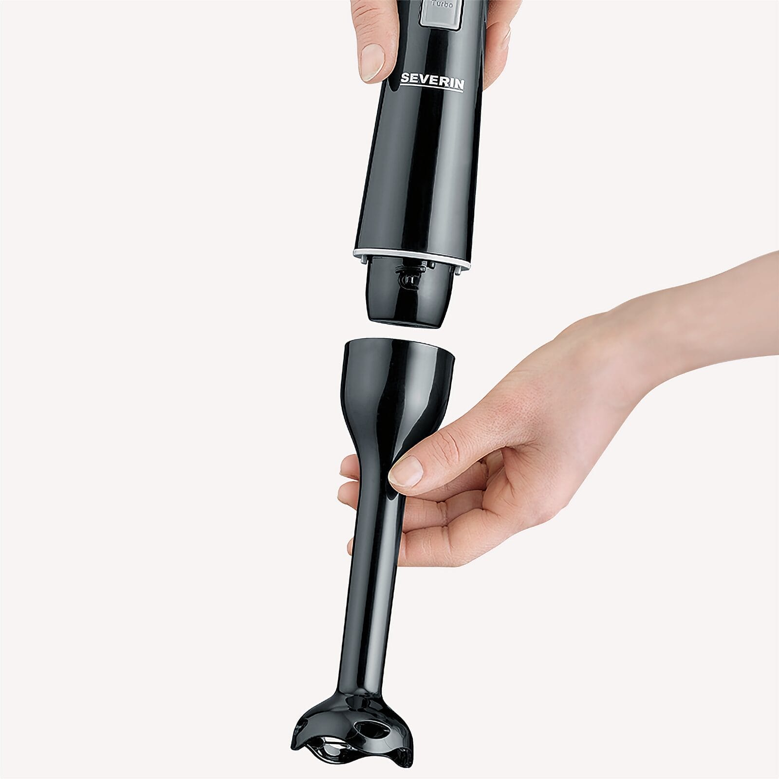 Jedna ręka trzyma czarną końcówkę blendera ręcznego, druga ją mocuje.