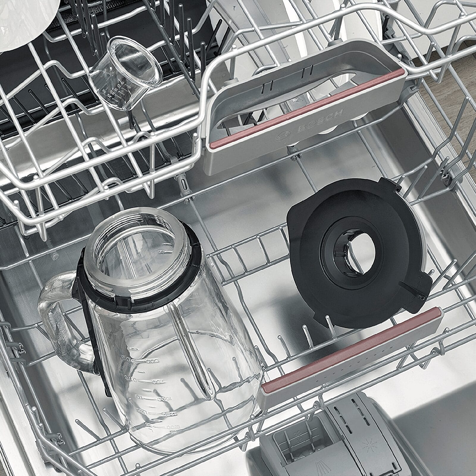 A glass pitcher and a black lid inside a dishwasher.