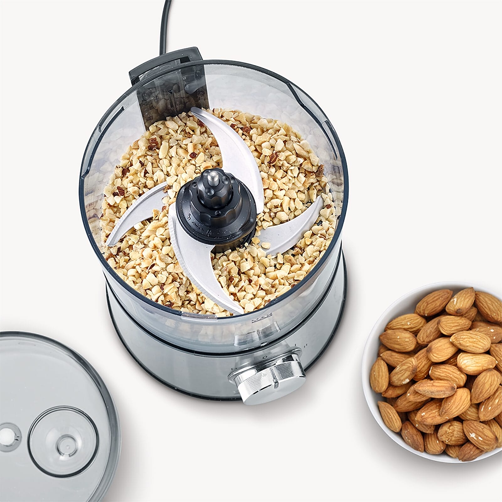 Ein Food Processor mit gehackten Nüssen und eine Schale Mandeln daneben.
