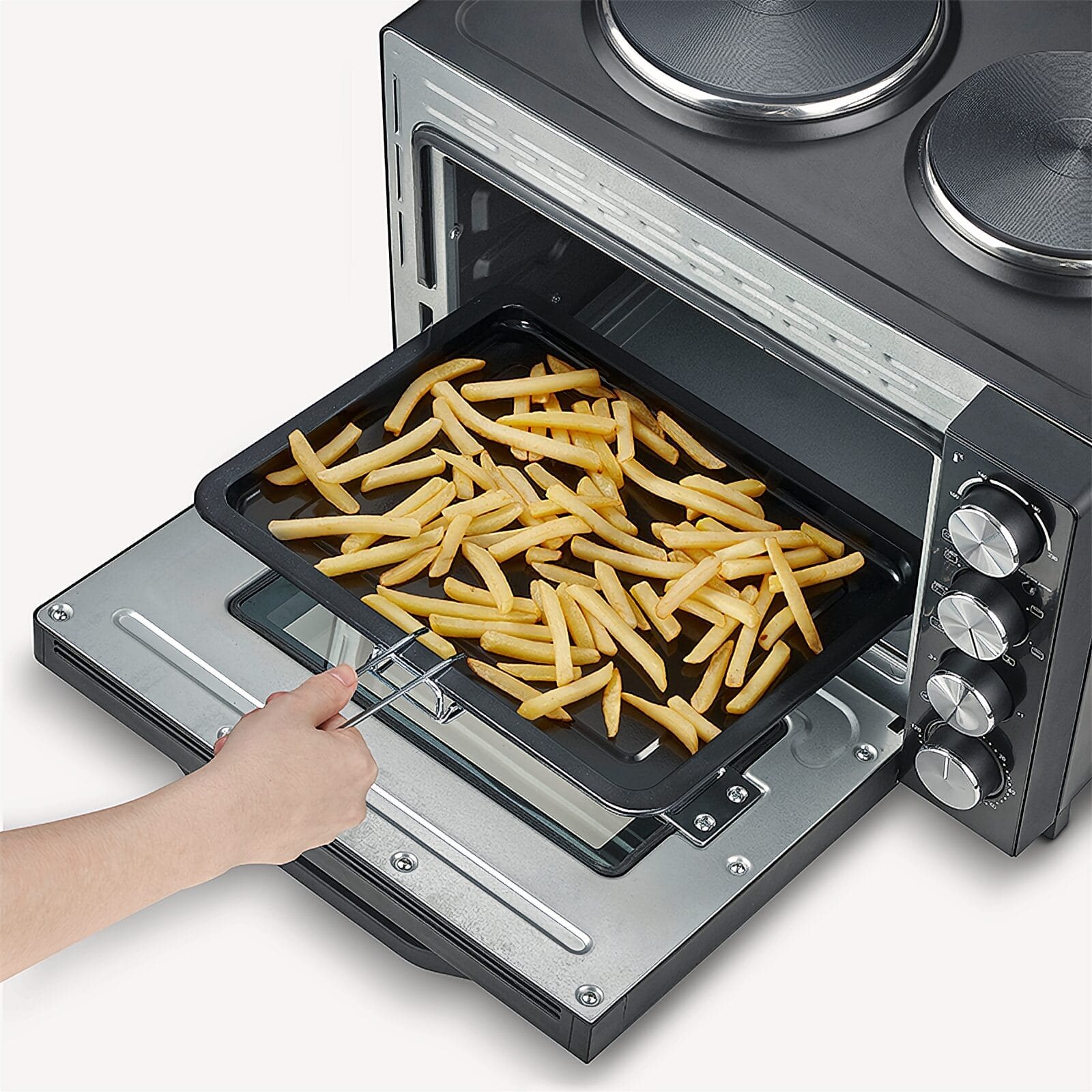 Une main glisse une plaque noire remplie de frites dans un four grille-pain.