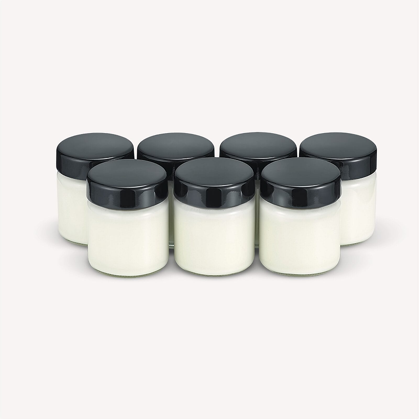 Zeven kleine potjes gevuld met witte crème en zwarte deksels op witte achtergrond.