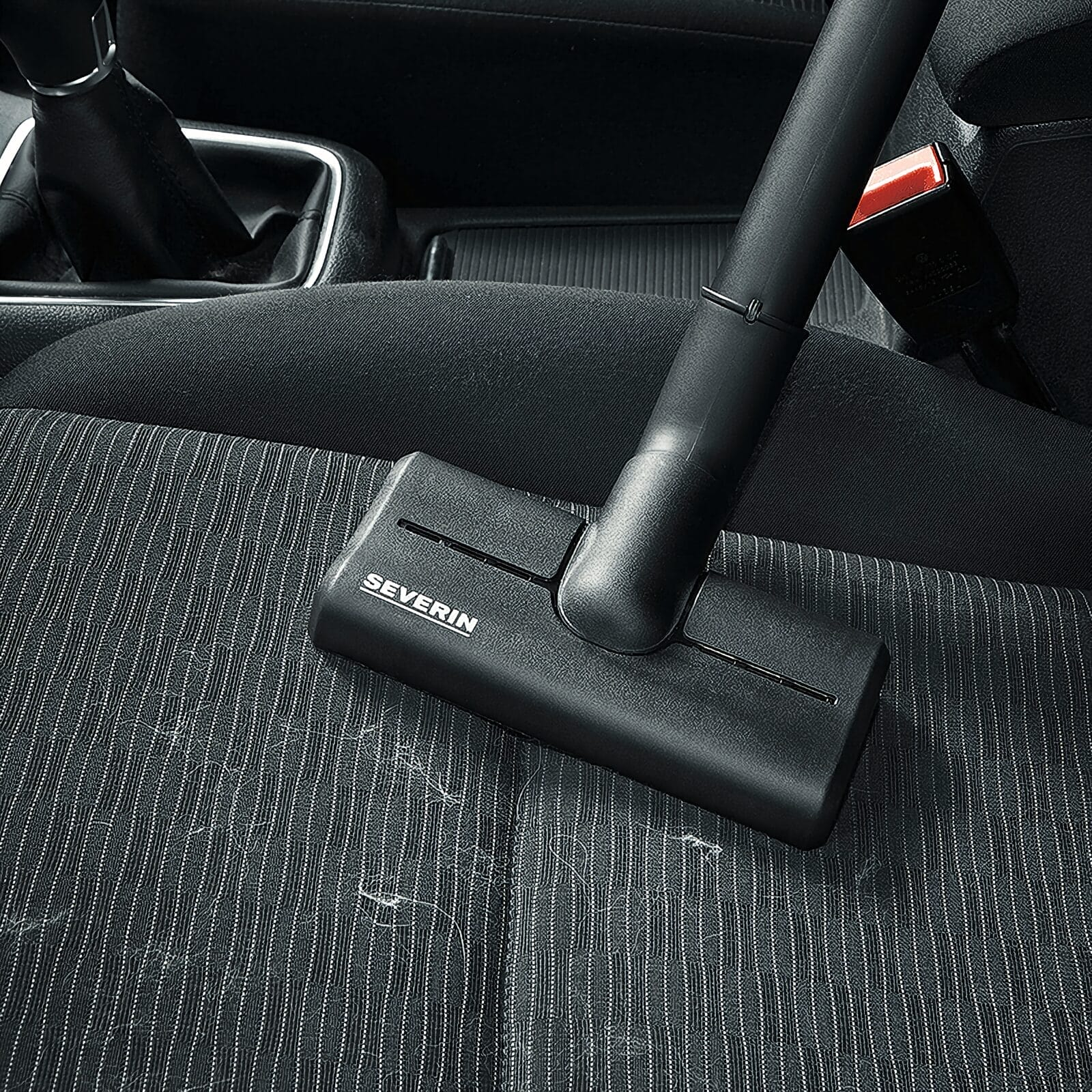 Głowica odkurzacza czyści tapicerowane siedzenie samochodu w paski.