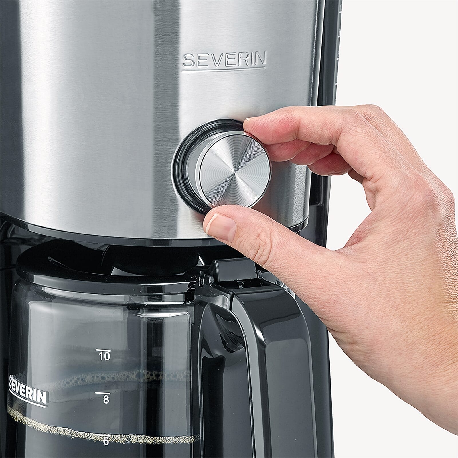 Dłoń obraca srebrne pokrętło ekspresu do kawy Severin. Widoczny jest dzbanek.