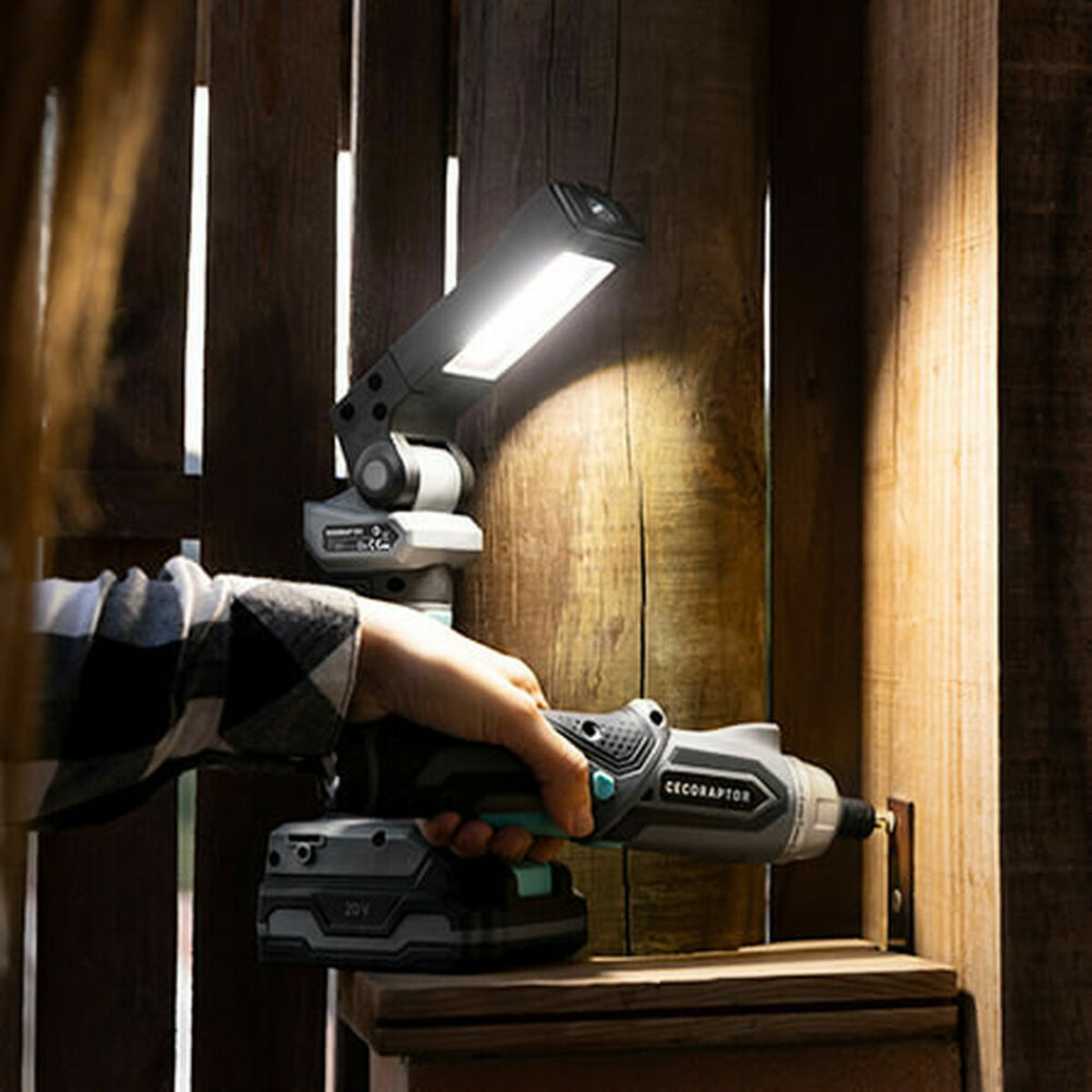 Dłoń trzyma szary wkrętarkę akumulatorową, oświetlając drewnianą powierzchnię jasnym światłem roboczym LED.