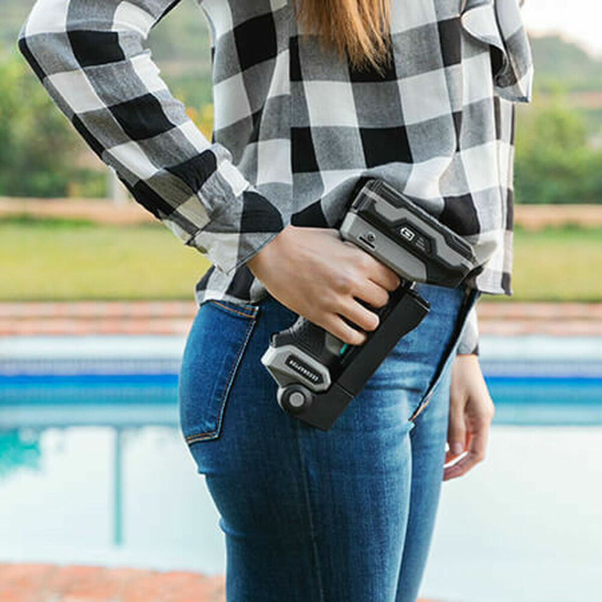 Osoba w dżinsach i koszuli w kratę trzyma narzędzie przy basenie.