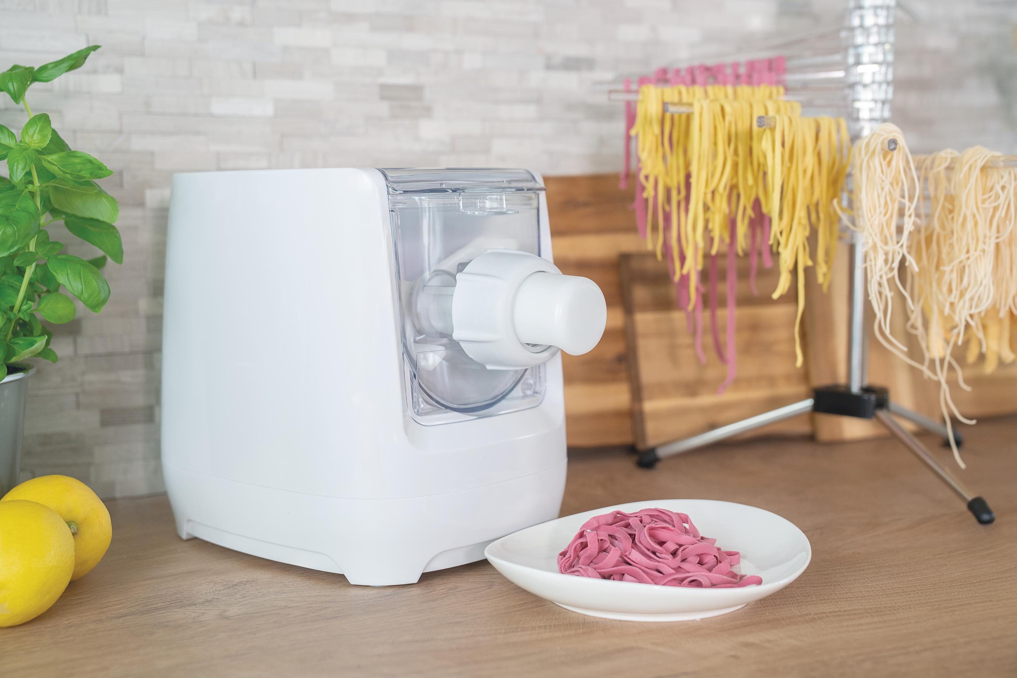 Eine weiße Nudelmaschine mit pinken Nudeln auf einem Teller und Nudeln zum Trocknen.