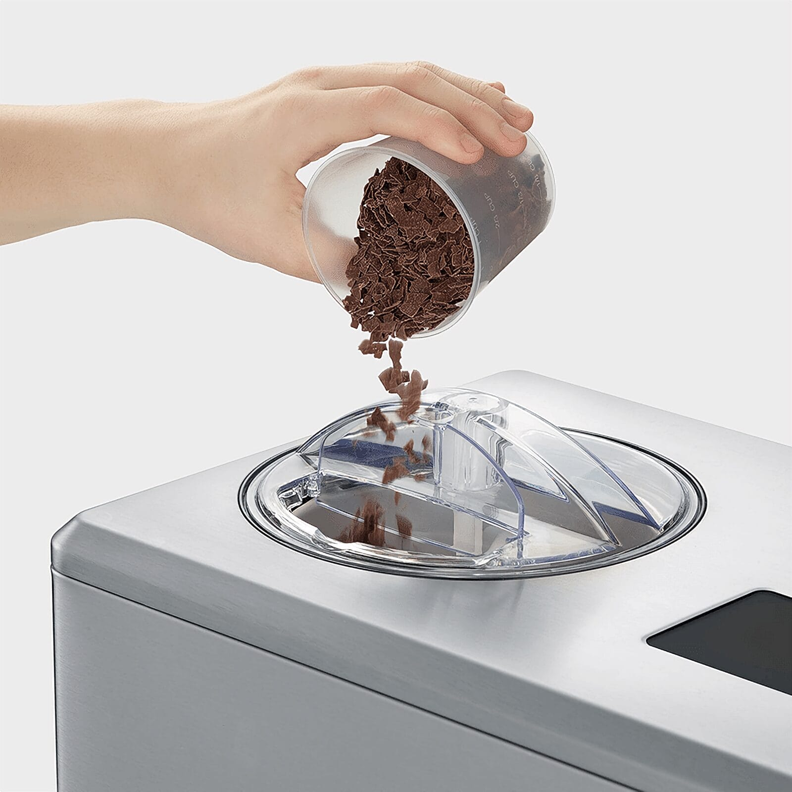 Una mano vierte trozos de chocolate de una taza en una máquina de helados.