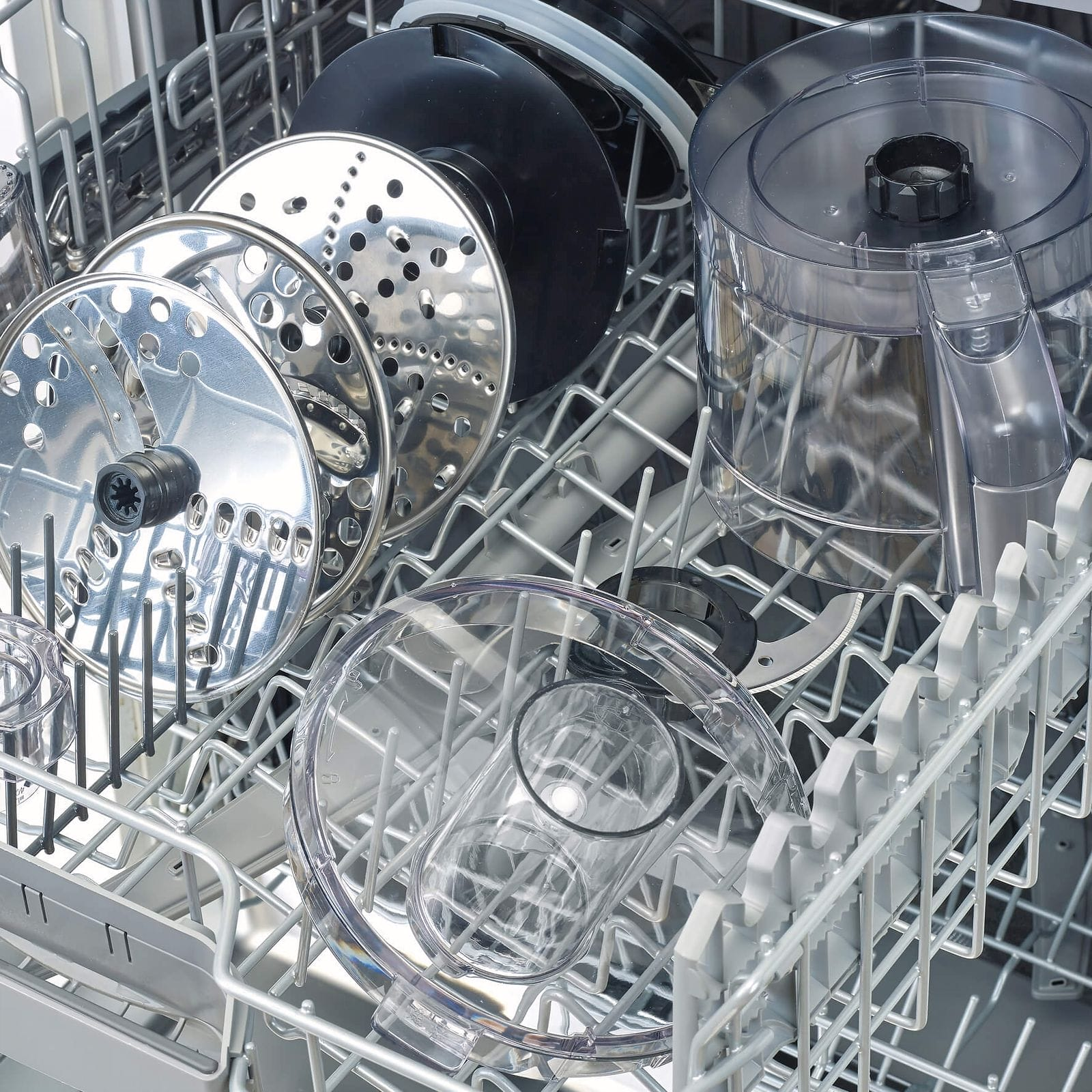 Keukenmachine-accessoires en schijven in een vaatwasmand.