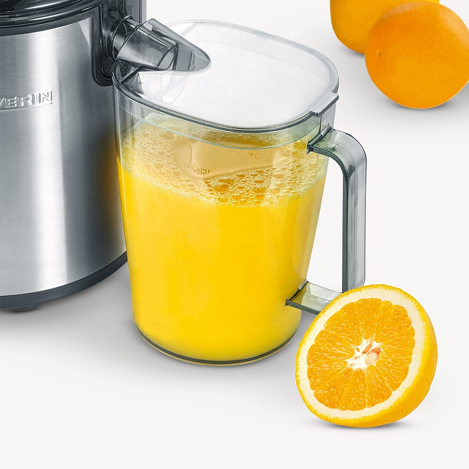 Un estrattore di succo con una caraffa piena di succo d'arancia e arance.